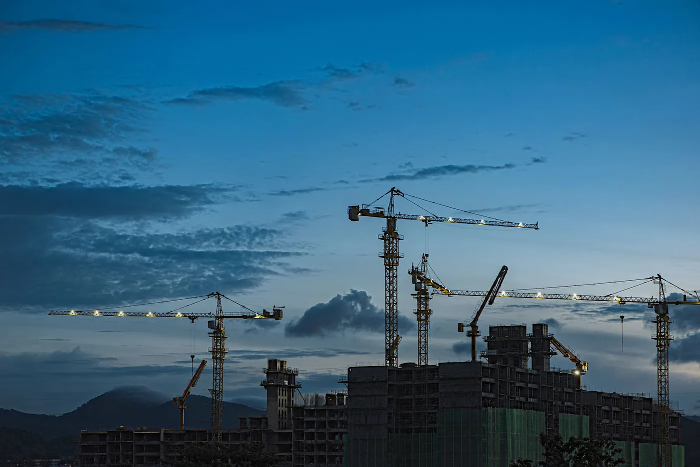 Tower cranes lit up over a building site at dusk