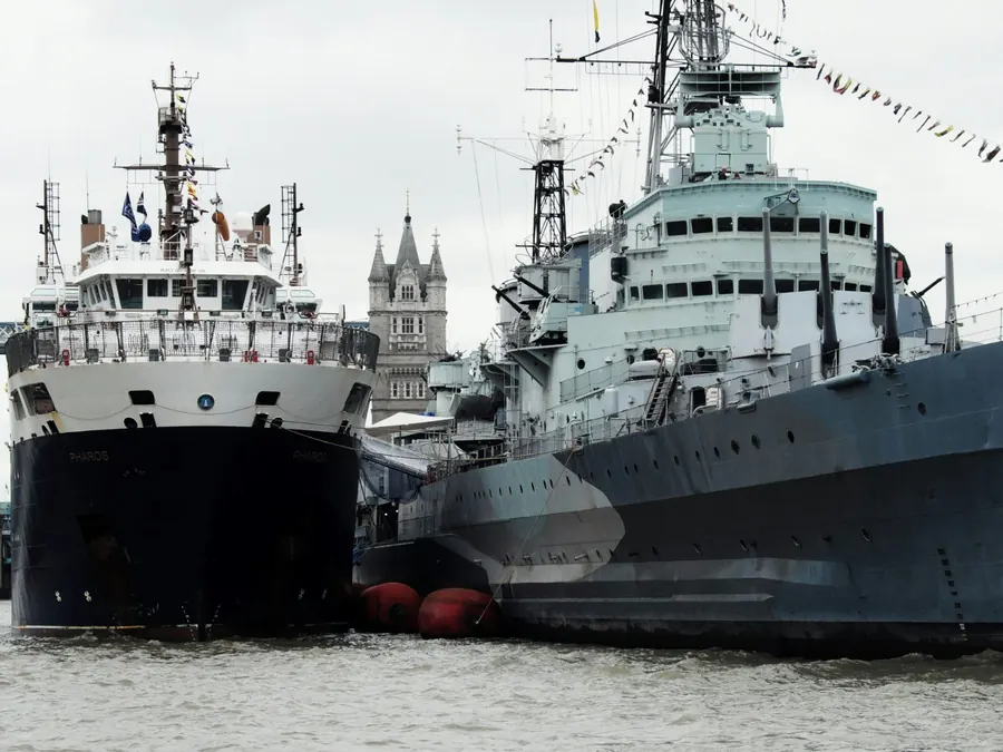 A grey warship and a second vessel moored on the Thames near Tower Bridge